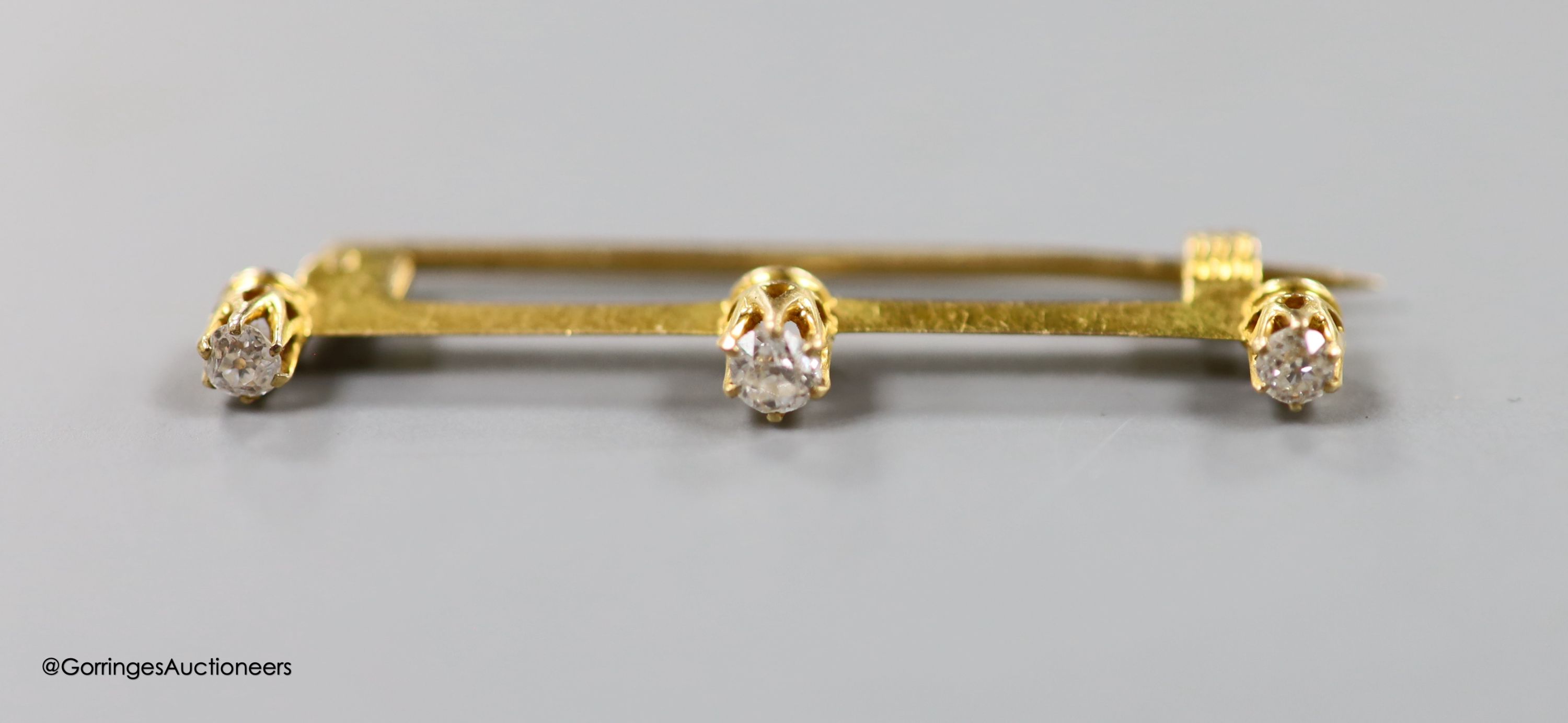 An early 20th century yellow metal and three stone diamond set bar brooch, 36mm, gross 1.6 grams and a yellow metal and simulated pearl set neck chain, 47cm, gross3.8 grams.